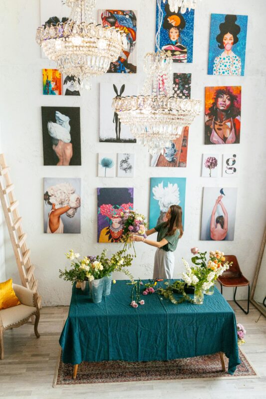 A woman arranging flowers in a modern art gallery setting with vibrant wall paintings.