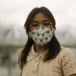 Teenage girl with eyeglasses wearing a patterned face mask outside.