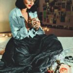 Woman enjoying coffee in a cozy room with flowers and soft lighting.