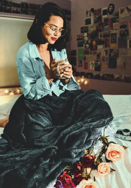 Woman enjoying coffee in a cozy room with flowers and soft lighting.