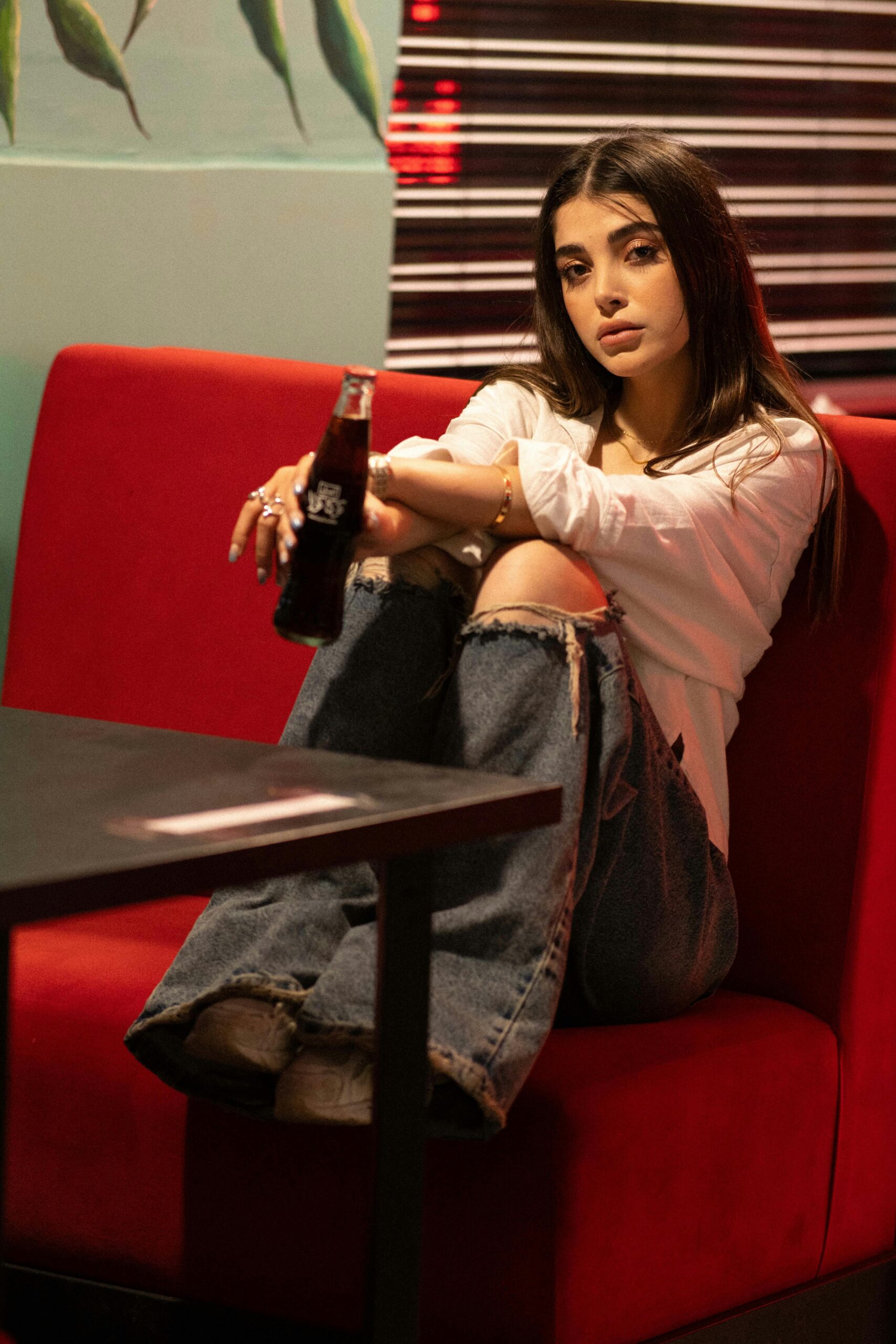 Stylish woman seated in a cafe with a relaxed pose, holding a drink. Modern and cozy vibe.