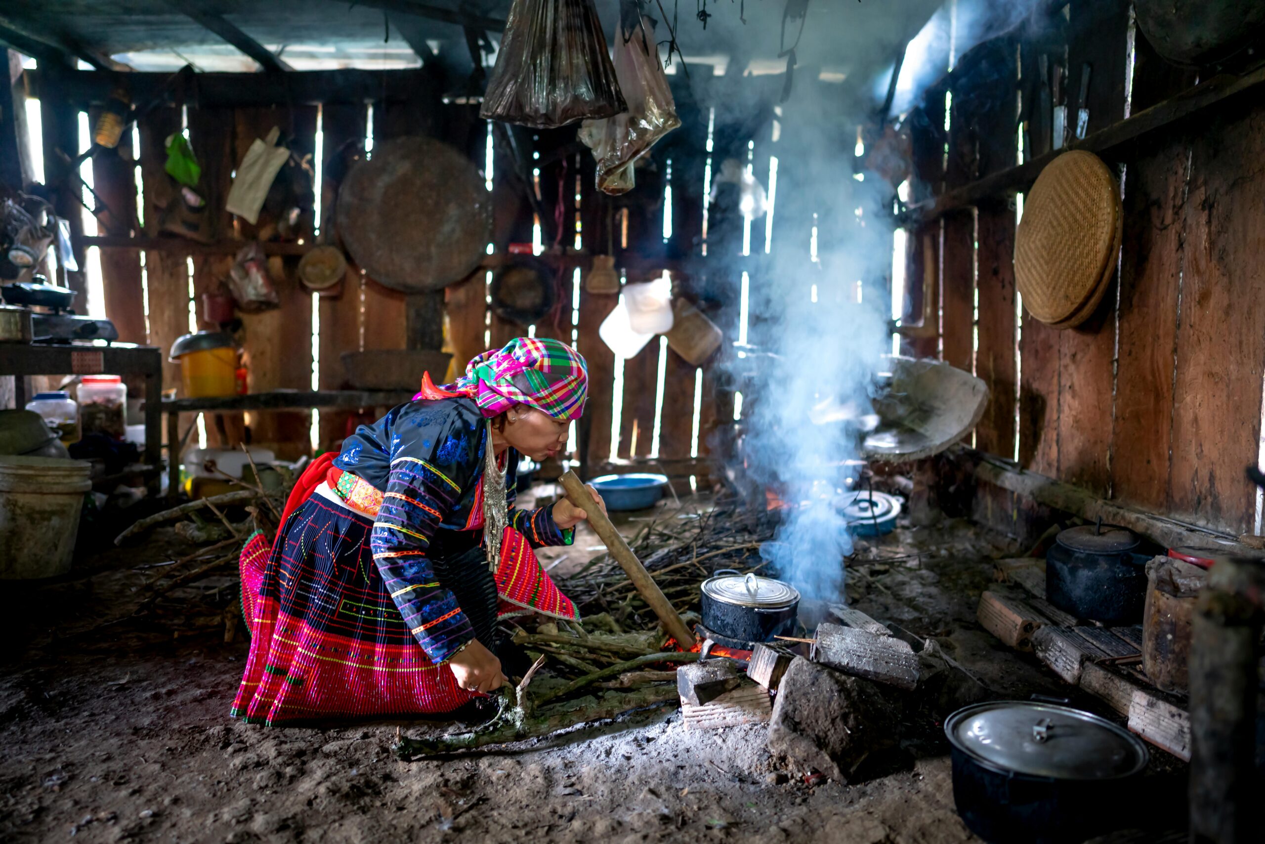 pexels-photo-4553565-4553565 A woman in traditional attire cooking on an open fire in a rustic rural kitchen.