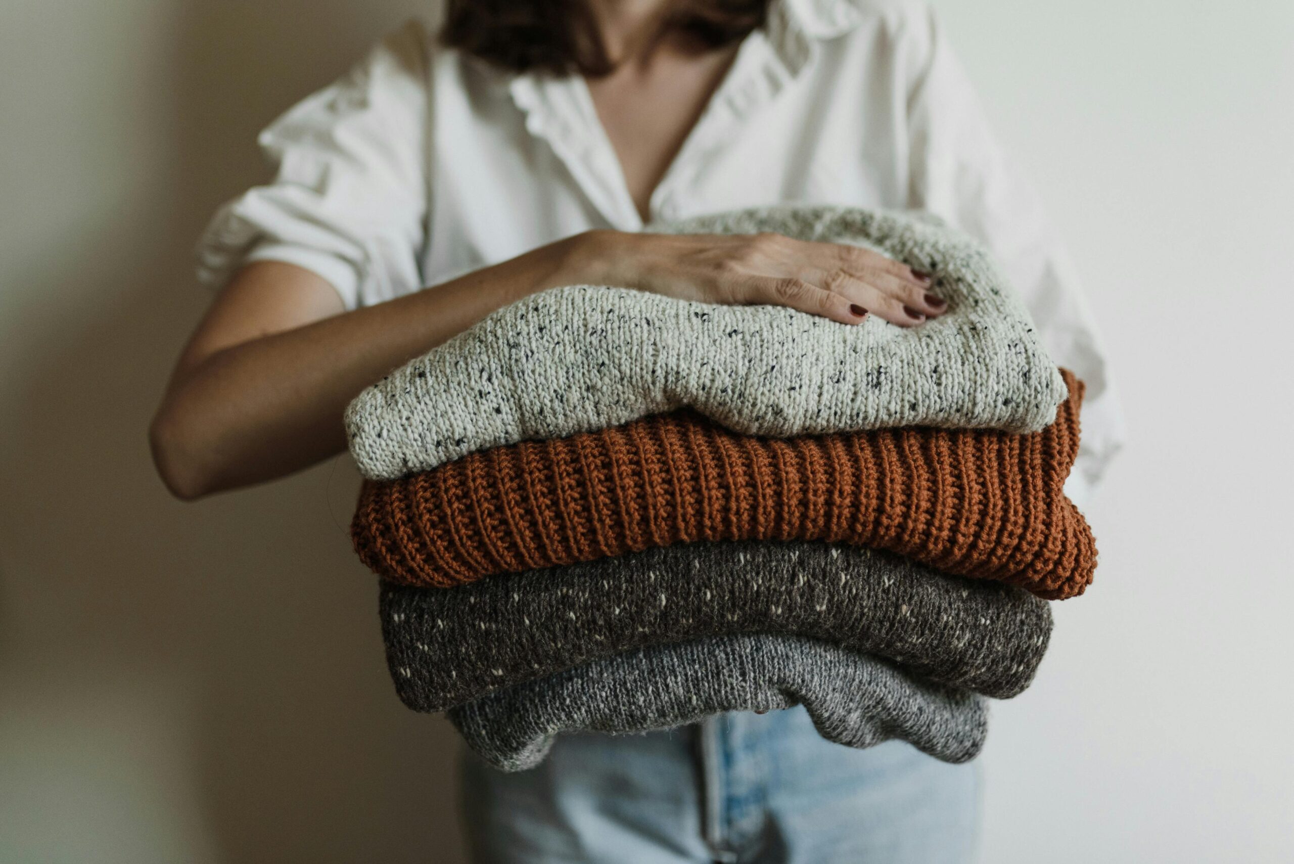 pexels-photo-5710033-5710033 A woman holding a stack of cozy, warm knit sweaters, perfect for winter.