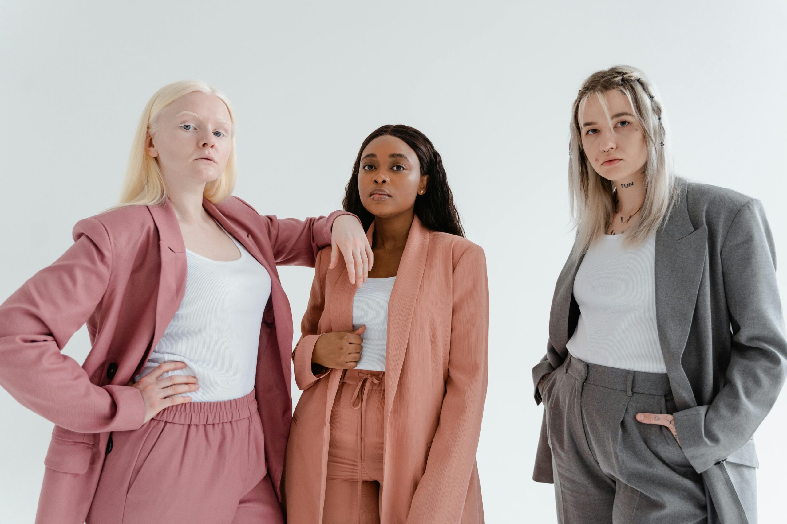 Three diverse women in trendy business suits pose confidently against a white background.