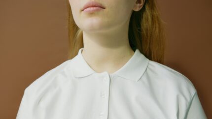 Minimalist close-up photo of a woman in a white polo shirt with a neutral background.