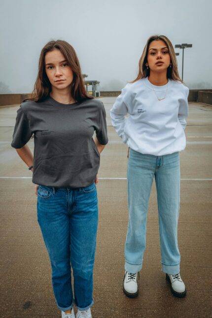 Two young women standing confidently in casual streetwear outfits on an overcast day.