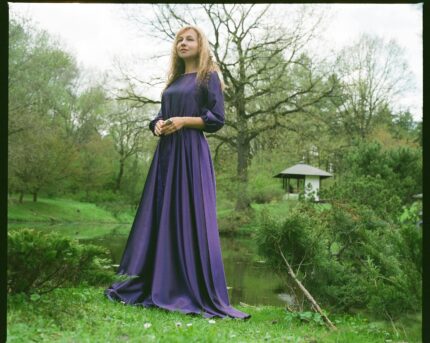 A serene portrait of a woman in a flowing purple gown against a lush spring park backdrop.