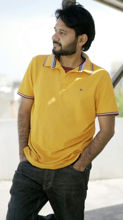 Portrait of an adult man in a yellow polo shirt standing outdoors, looking contemplative and relaxed.