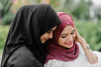 Side view content young Muslim females wearing traditional hijab resting in city park together and smiling