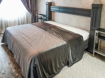 Cozy bedroom featuring a stylish gray comforter, ornate headboard, and rustic flooring.